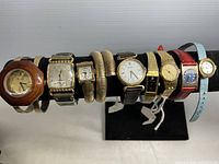Full view of nine vintage watches displayed on a black stand showing various styles, bands and colors.