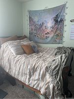 Side view of queen size bed with striped linens, pillows, tapestry and string lights visible