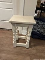 Side view of white wooden stool showing turned legs and support bars on the floor