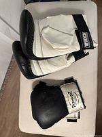 Pair of TKO boxing gloves in black and white with Velcro wrist straps resting on a surface.