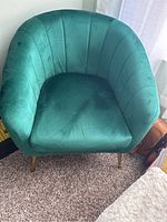 Front facing view of green velvet chair showing channel tufting and gold tapered legs on carpeted floor