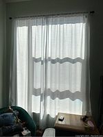 Sheer white curtains hanging from the rod, sunlight filtering through and casting shadows on them.