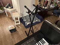 Photo showing the black X-style adjustable metal keyboard stand and partial view of keyboard in a room with hardwood floor.