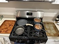Four pots and pans and two baking sheets arranged on and beside a stove.
