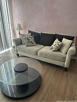 Beige fabric couch with cushions against a wall, positioned next to vertical blinds on a window.