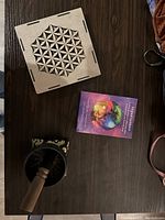 Top view of closed wooden box with flower of life design, metal singing bowl with wooden mallet, and angel cards deck on wooden surface.