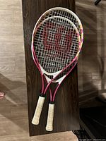 Photo showing two Wilson tennis rackets on a wooden surface, highlighting the color and string details.
