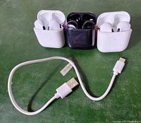 Photo of three pairs of Blackweb Bluetooth earbuds in charging cases, two white and one black, plus one white USB charging cable.