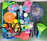 Photo showing various new outdoor sports accessories including badminton rackets, catch ball paddles, plastic balls, frisbee, jump ropes and shuttlecocks.