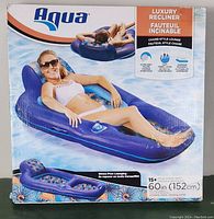 Front view of Aqua Luxury Recliner box showing chaise-style inflatable lounge with a woman reclining in water. Shows ultra-soft pillow, soft fabric cover, and superior buoyancy features.