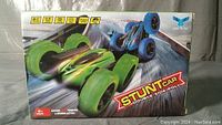 Front view of the product box showing the green and blue stunt cars, highlighting the stunt car's double side roll feature and the 2.4 GHz remote control system. The packaging states it is suitable for ages 6 and up and focuses on extreme stunt spinning action.