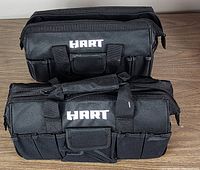 Two black Hart duffel bags stacked on a wooden surface showing front with pockets and handle with brand name visible.
