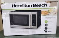 Box of the Hamilton Beach microwave showing distressed packaging and product image with dimensions and capacity.