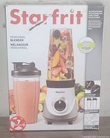 Box front showing Starfrit personal blender with a blending jar filled with fruit and one blending cup with smoothie content.