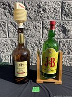 Photo showing Seagram's V.O. bottle dispenser with white accordion spout and J&B Rare Scotch Whisky bottle dispenser on wooden stand