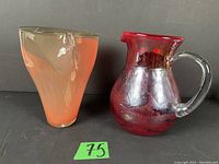 Front view of both the orange twisted vase and red pitcher with clear handle against dark background