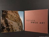 Front view of the book opened with slipcase showing the rock art image on the inside cover spread and the brown slipcase with black title text 'NEVADA ROCK ART'.