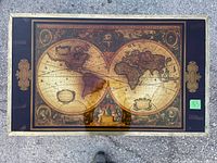Full view of the coffee table showing the brass frame, glass top with antique style world map beneath and campaign-style handles on sides.
