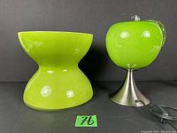 Photo showing side view of large green glass hourglass-shaped vase and green glass apple lamp on metal base.
