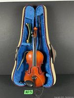 Full view of violin, bow, and accessories inside the hard protective case lined with blue fabric.