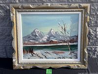 Full view of signed winterscape painting in ornate ivory carved frame, showing snow-covered mountains, bare tree, small cabin, and a river.