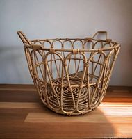 Large round rattan basket with open weave and handles on a wooden surface.