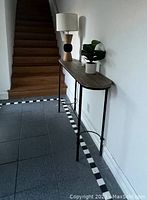 Console table placed along a wall near stairs, with a lamp and a potted plant on top.