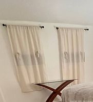 Pair of light beige curtains hanging on black rods over windows with a glass table below