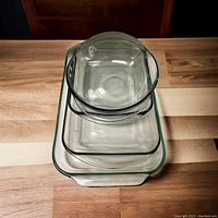 Three nested rectangular glass casserole dishes and a small round glass bowl stacked on a wooden surface.