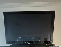 Front view of a large black Panasonic flat screen TV, screen off reflecting surroundings.