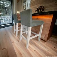 Side view of two green fabric upholstered bar stools with white wooden legs set next to a counter.