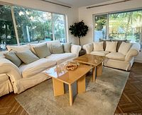 Two white upholstered sofas and ottoman in a living room setting with pillows and coffee tables.