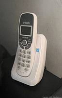Front view of white VTech cordless phone in base station showing keypad and LCD screen.