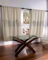 Dark wood coffee table with curved legs and rectangular glass top in front of beige curtains