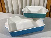 Two ceramic casserole dishes stacked, one medium size and one smaller size, blue exterior and white interior.