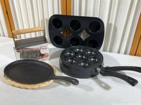 Overall view of the cast iron kitchen items: bacon grill press in box, two Nordic Ware pans for ebelskivers and popovers, and a cast iron fajita skillet.