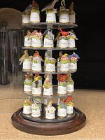 Close-up of multi-tiered plastic shelving holding 50 ceramic thimbles each topped with colorful miniature birds representing 50 states, on a wooden base.