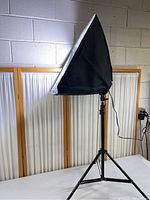 Full view of black tripod light stand with attached softbox light, setup indoors near wall.