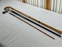 Three walking canes laid side by side, showing different lengths and materials including bamboo, black lacquered wood, and dark wood with inlay.