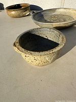 Three handcrafted pottery bowls placed outdoors in sunlight showing varying glaze patterns and sizes.