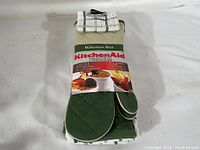 Front view of KitchenAid oven mitts and kitchen towels still in original packaging showing label and product details.