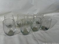 Eight clear Mikasa Cheers stemless wine glasses with assorted etched mid-century modern patterns shown from a top-down angle on a white cloth background.
