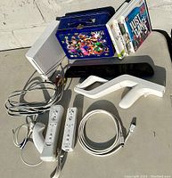 Photo of Nintendo Wii console with sensor bar, two Wii remotes, Nunchuk, cables, three game cases, and Mario-themed lunchbox.