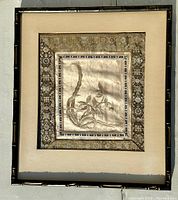 Front view of the framed silk tapestry showing floral silk textile art with intricate metallic thread border and black bamboo-style frame.
