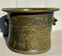Side view of signed stoneware planter showing green glaze, textured design, and looped handles.