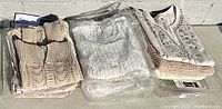View of various folded knit sweaters and shirts in light neutral colors including beige, white, and cream, with some packaged in plastic.