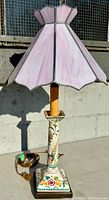 Table lamp with pink stained glass shade, ceramic base with colorful floral and bird design, on wooden base