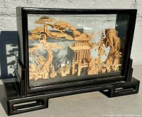 Front side view of the vintage Chinese cork carving diorama in glass case showing pagoda, tree, deer, rocky details and black wooden base.