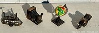 Four vintage diecast metal figural pencil sharpeners including a paddle wheeler ship, bellows camera, globe, and vintage camera, shown on a white surface in sunlight.