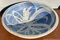 Photo of wide shallow pottery dish showing blue and oatmeal glaze decoration inside, with floral or abstract swirl pattern.